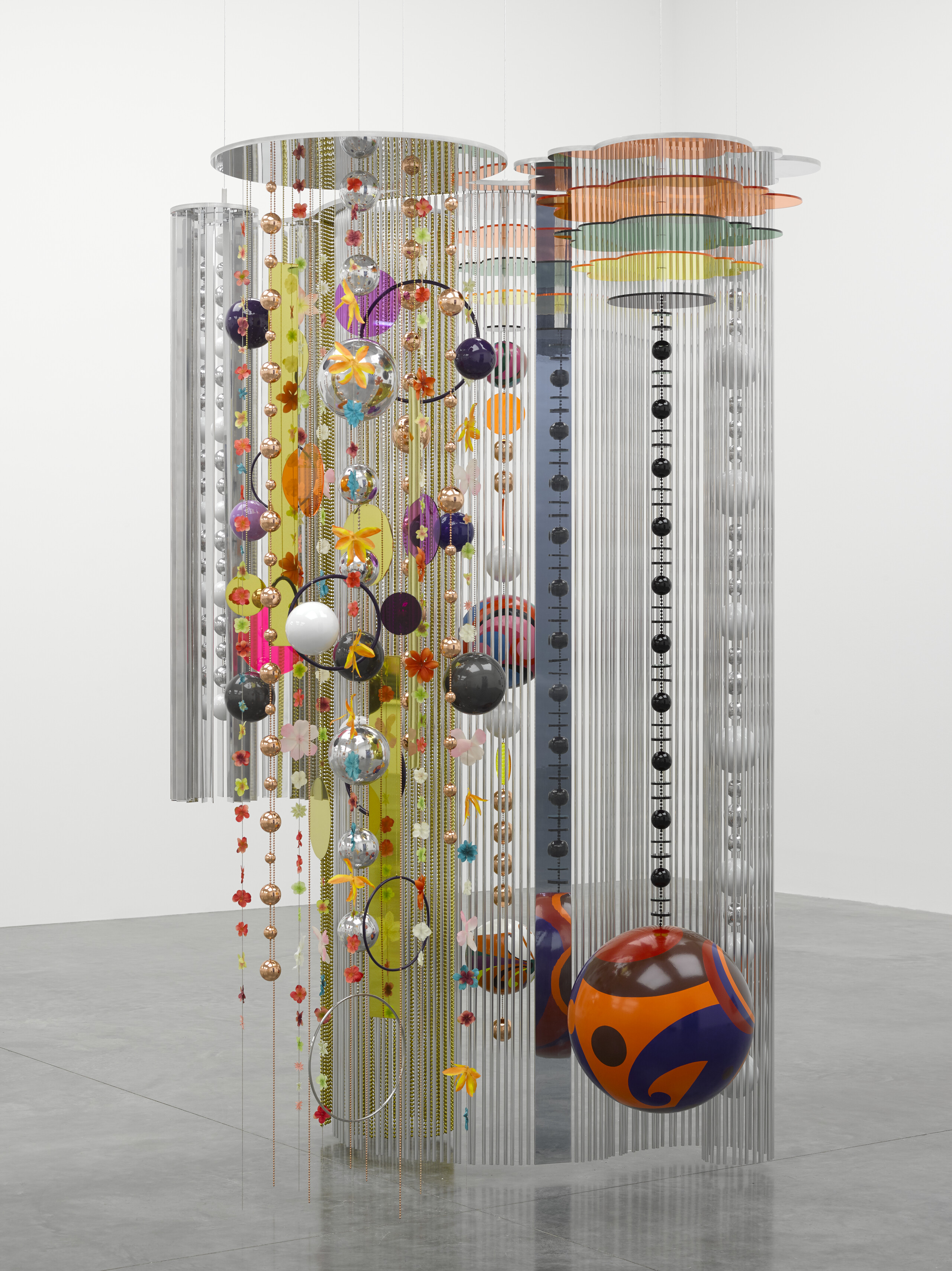 A sculpture hanging from a white ceiling made of many multi-colored chains, balls, beads, and circles.