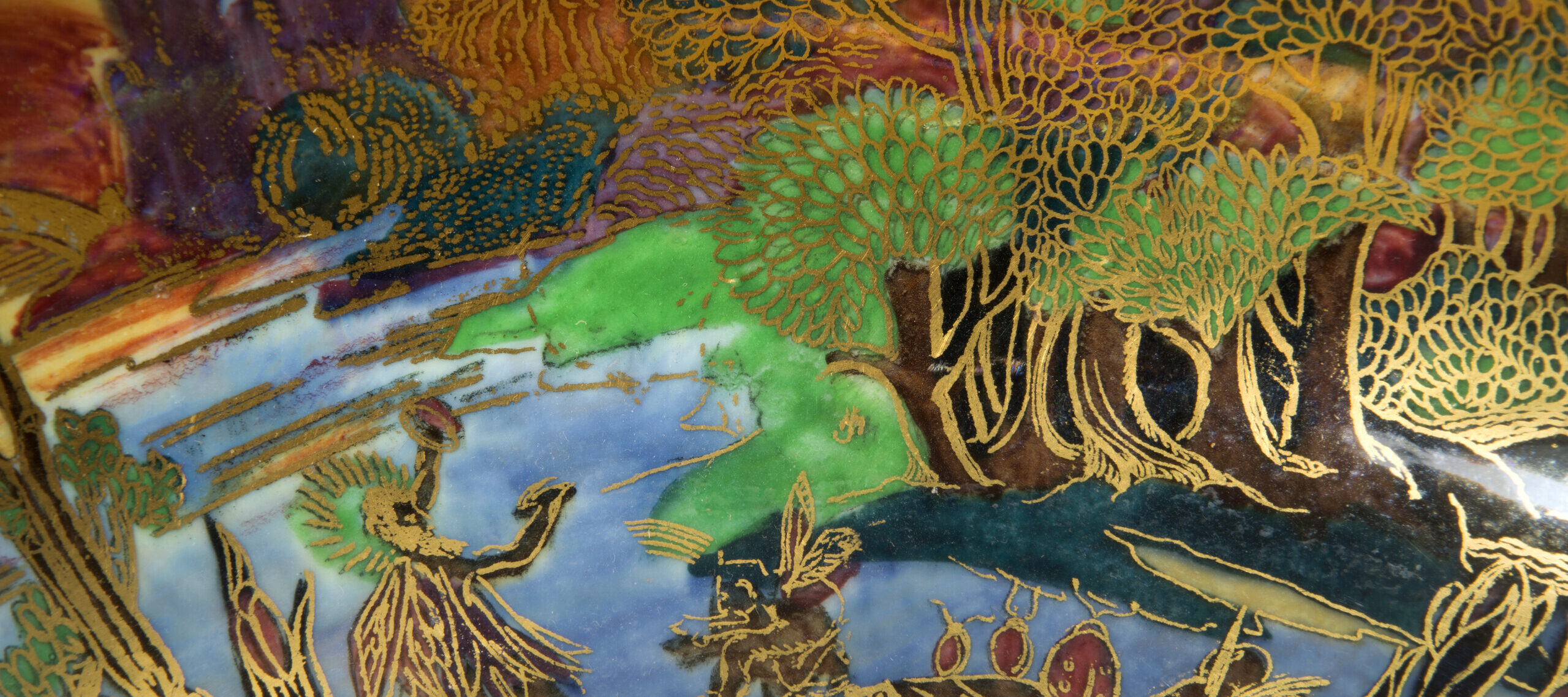 Detail image of a ceramic punchbowl painted with blue, green, red, and purple tones. The details of a mythological scene are painted in gold on top of the swaths of color.