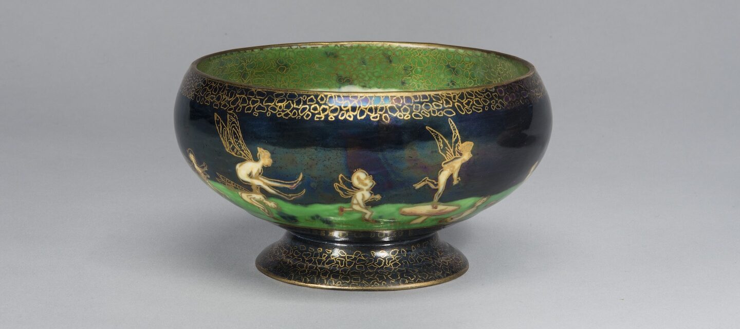 Porcelain pedestal bowl featuring an iridescent lustreware glaze. Around the bowl, winged fairies and sprites cavort on a vibrant green field set against a deep blue background. The figures and the decorative elements along the rim and foot of the bowl are outlined in gold cloisonne.