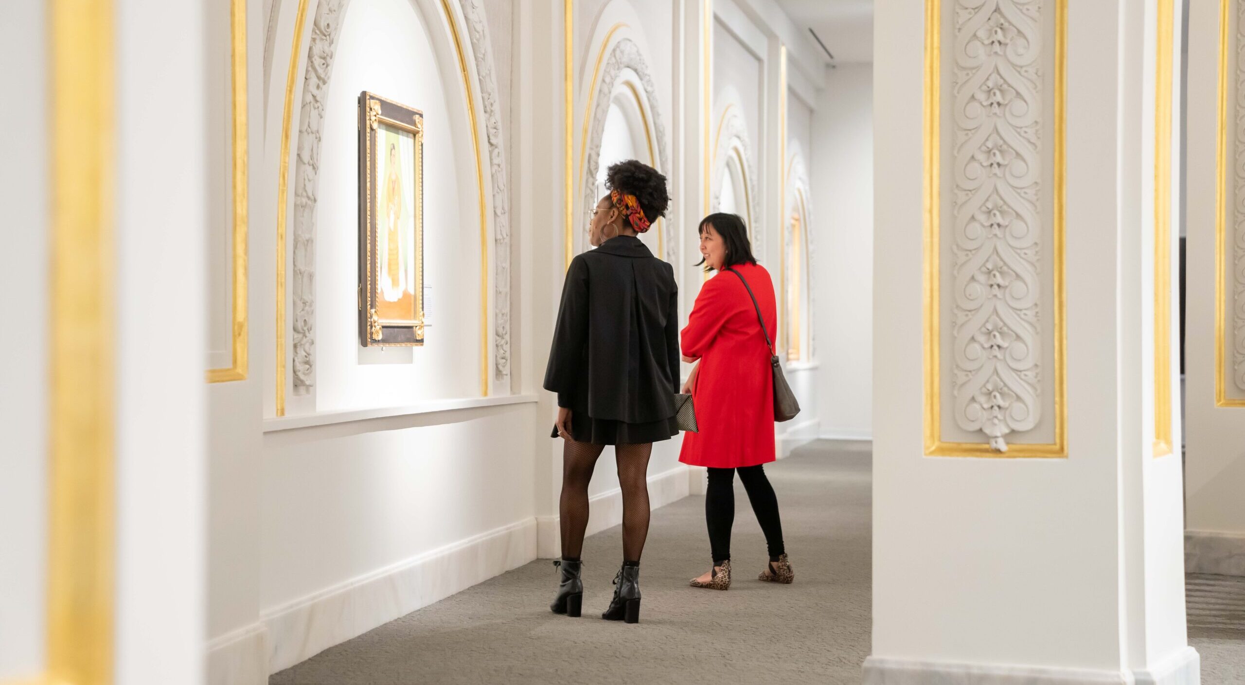 Two museum visitors observe artworks in a modern gallery.