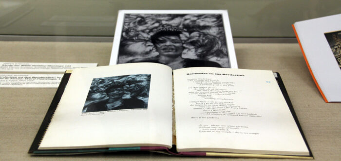 A book is lying in a glass case. The book shows text and a black-and-white photographic portrait of a woman's face.