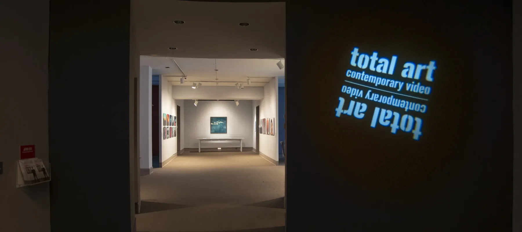 View of a gallery space. In a dark room, the title of the exhibition, "Total Art: Contemporary Video", is projected on a wall.