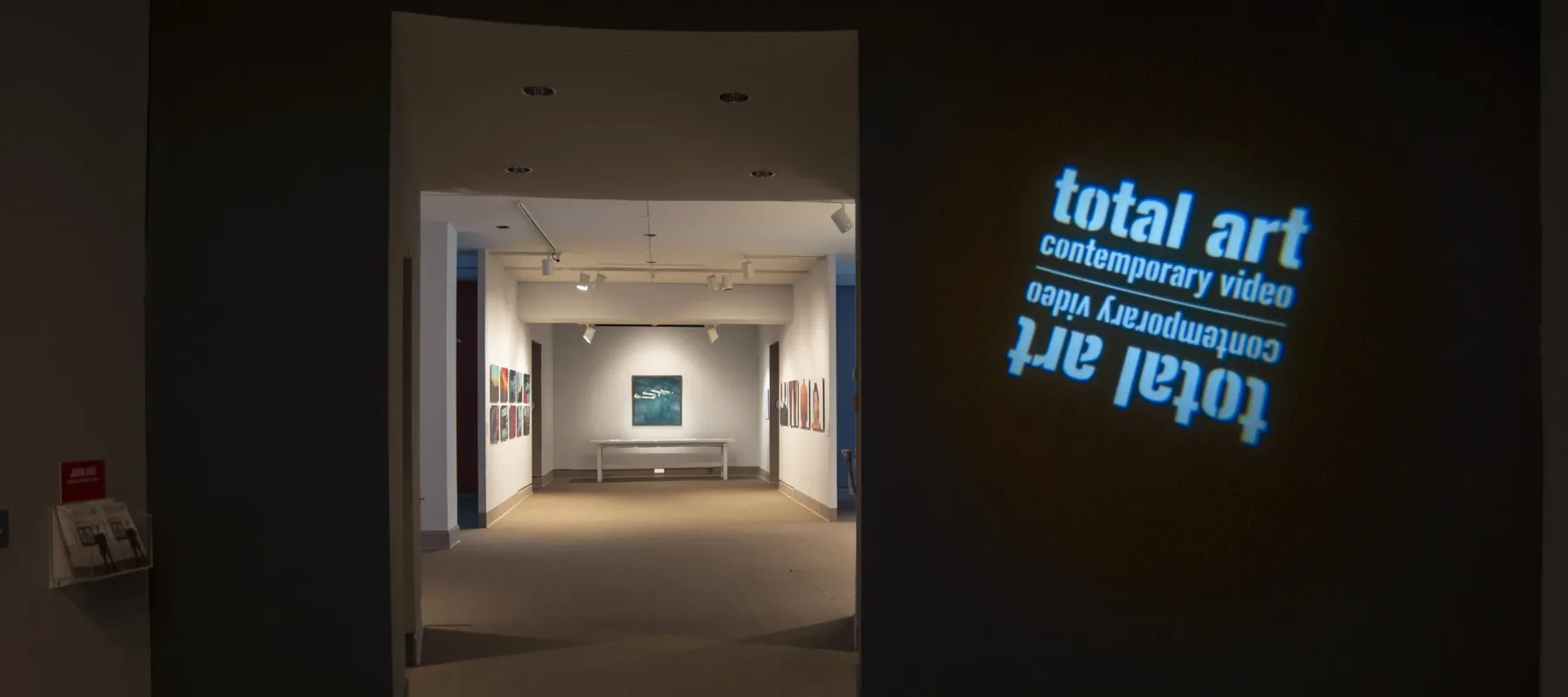 View of a gallery space. In a dark room, the title of the exhibition, "Total Art: Contemporary Video", is projected on a wall.