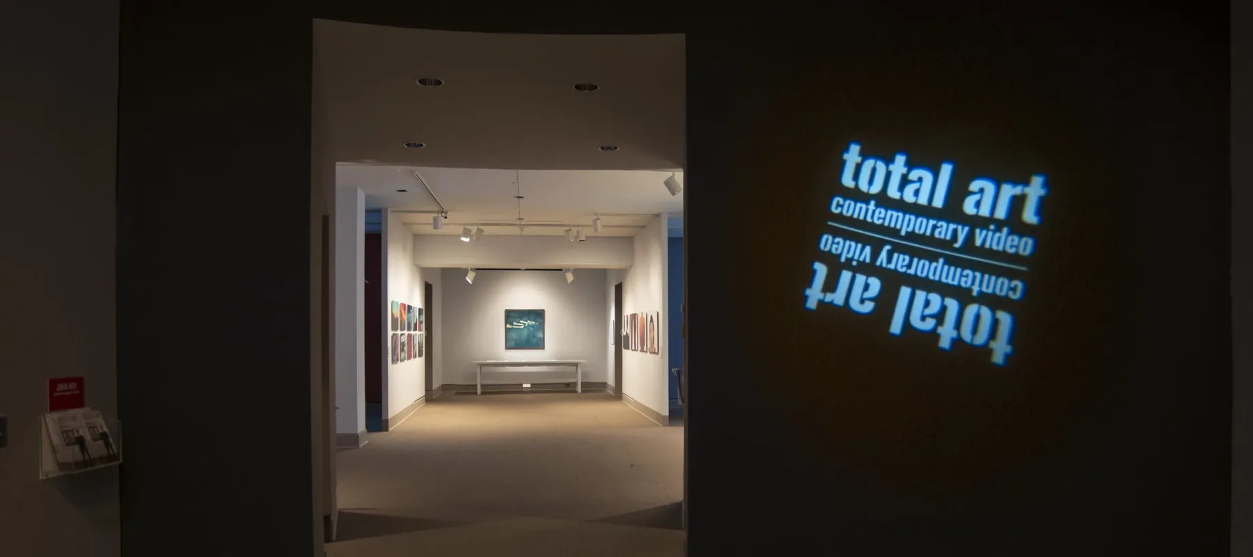 View of a gallery space. In a dark room, the title of the exhibition, "Total Art: Contemporary Video", is projected on a wall.