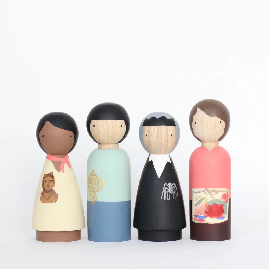 Four minimalist wooden dolls are arranged against a white background. They are painted wearing different sets of clothing and hair.