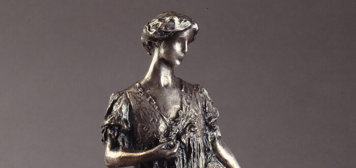Bronze sculpture of a standing woman gazing over her right shoulder, holding a fan by her side. She wears a long, loose gown that gathers at her feet, with her hair swept off her neck. Her left hand holds a flower by her bust.