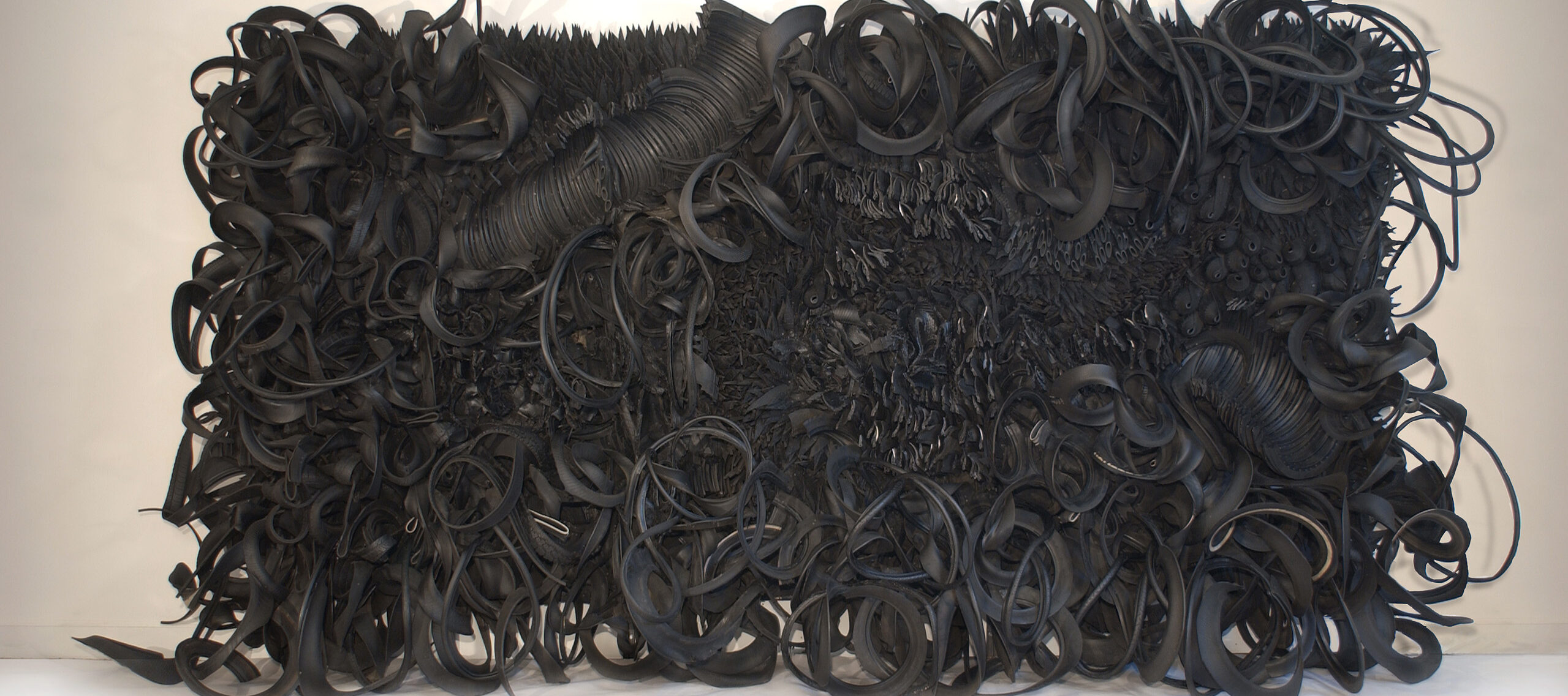 The wall-sized, horizontal sculpture consists of black rubber tires and tubing that has been sliced, stripped, woven, looped, twisted and otherwise manipulated into an expressive and abstract high-relief tableau.