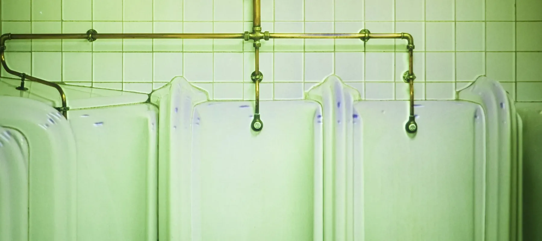 A photograph of the interior of a bathroom showing several urinals. The photograph is tinted in green.