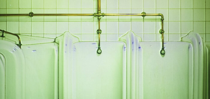 A photograph of the interior of a bathroom showing several urinals. The photograph is tinted in green.