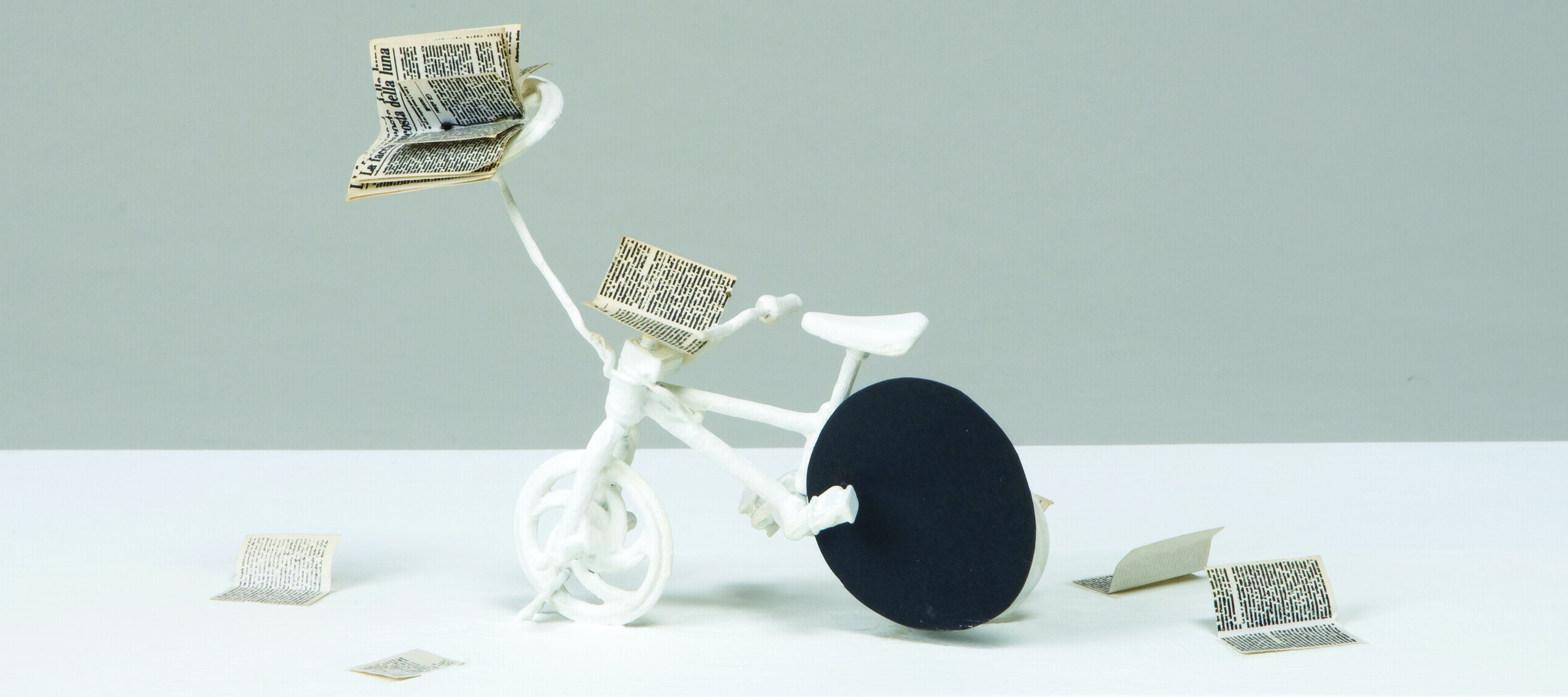 A tiny bicycle sculpture with a tiny book attached to it, as well as several books lying next to it.