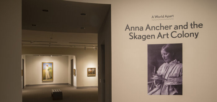 View of a gallery space. On a white wall, it says "A World Apart: Anna Ancher and the Skagen Art Colony."