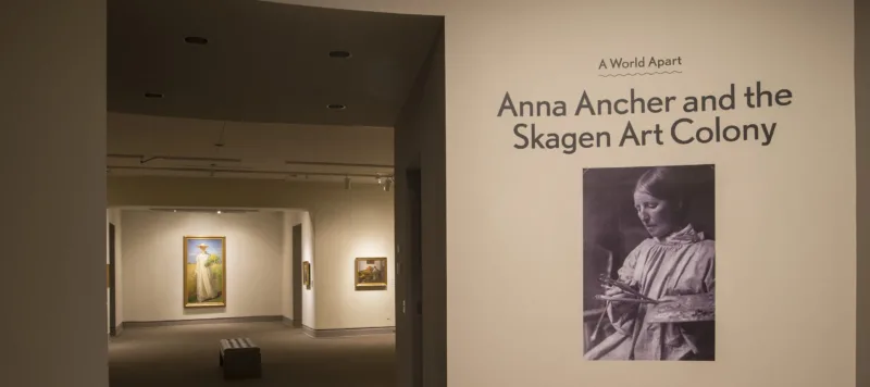 View of a gallery space. On a white wall, it says "A World Apart: Anna Ancher and the Skagen Art Colony."