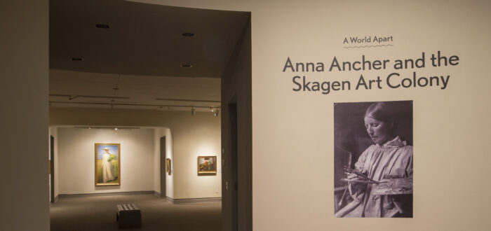 View of a gallery space. On a white wall, it says "A World Apart: Anna Ancher and the Skagen Art Colony."