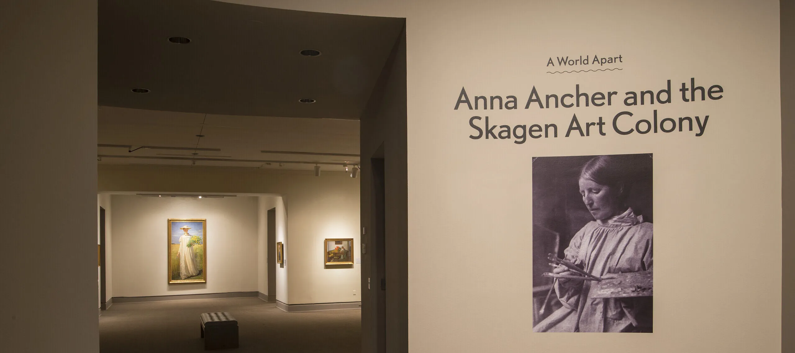 View of a gallery space. On a white wall, it says "A World Apart: Anna Ancher and the Skagen Art Colony."