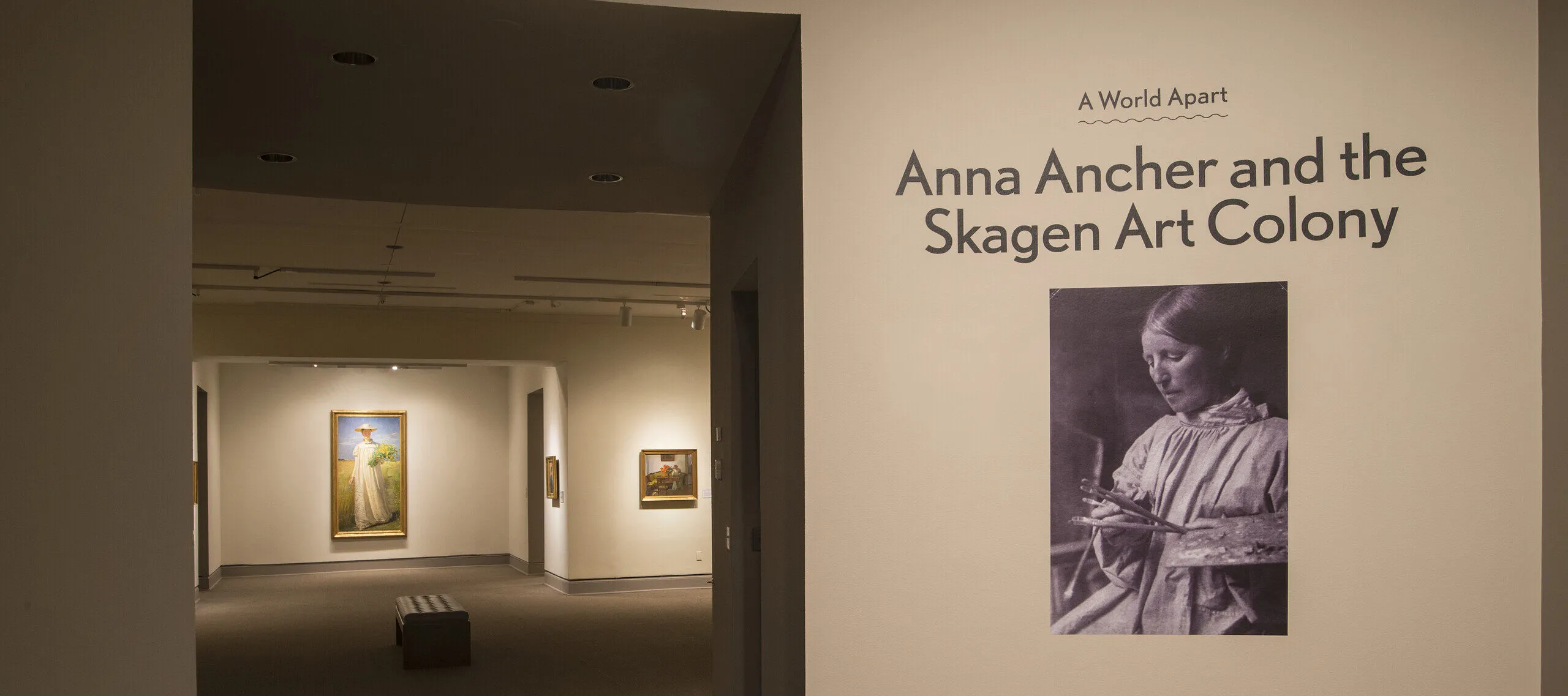 View of a gallery space. On a white wall, it says "A World Apart: Anna Ancher and the Skagen Art Colony."