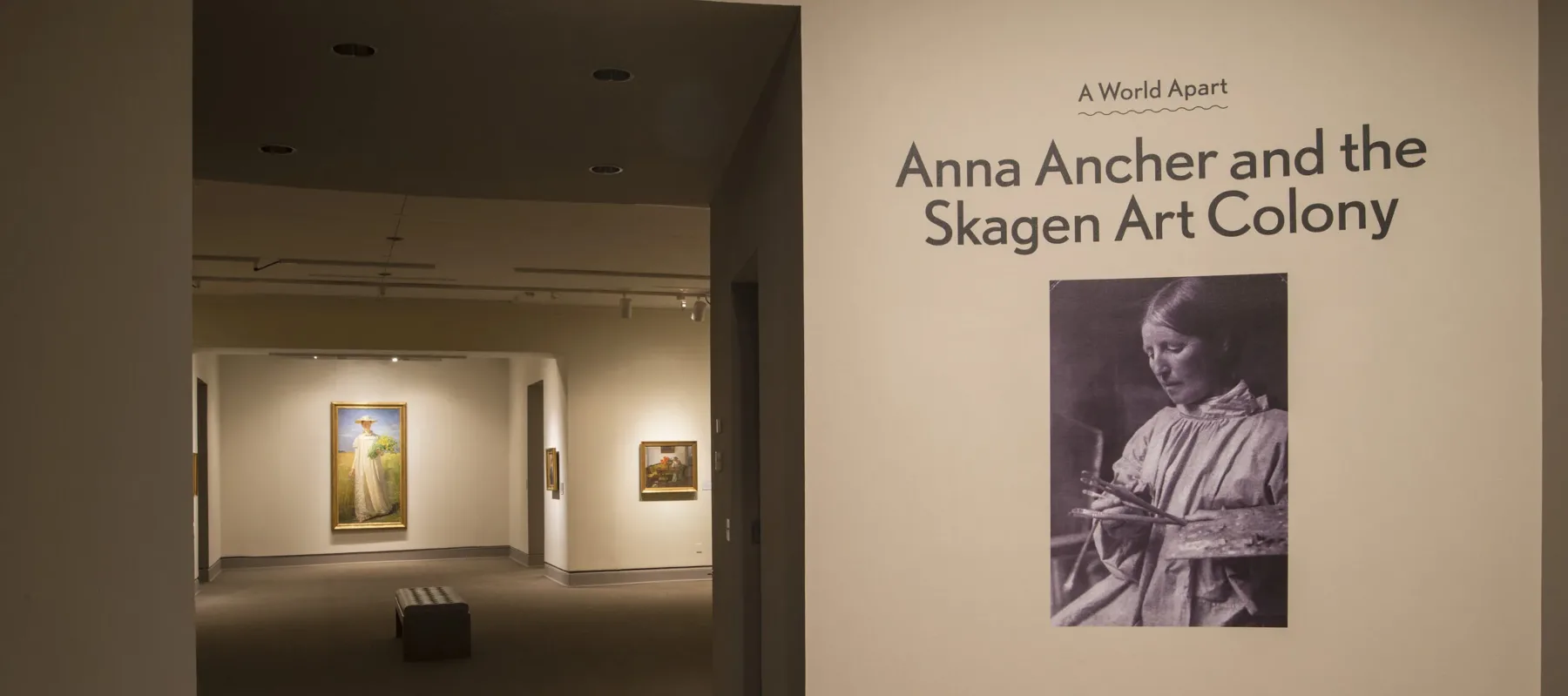 View of a gallery space. On a white wall, it says "A World Apart: Anna Ancher and the Skagen Art Colony."