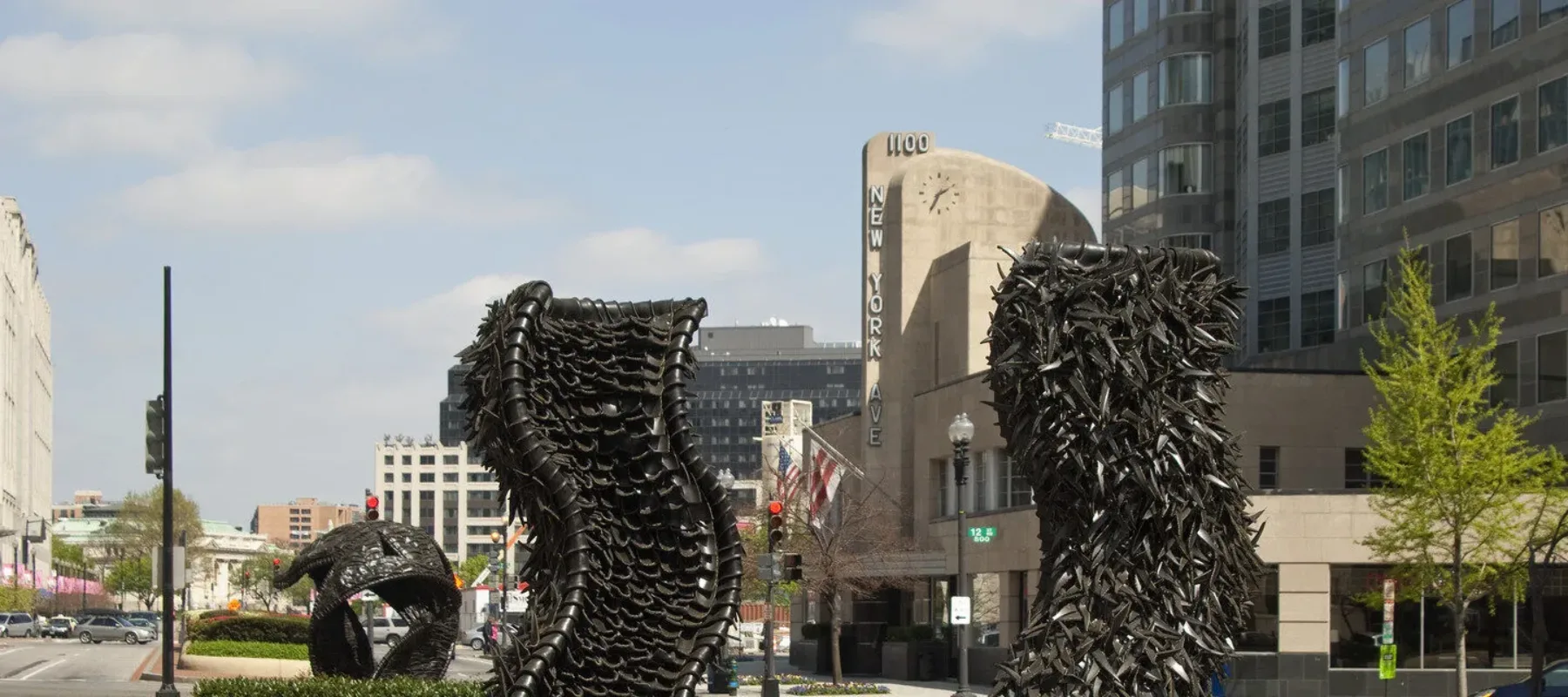 Two large abstract sculptures made from tires rise from a center median in a city street. The sculptures are wavy columns.