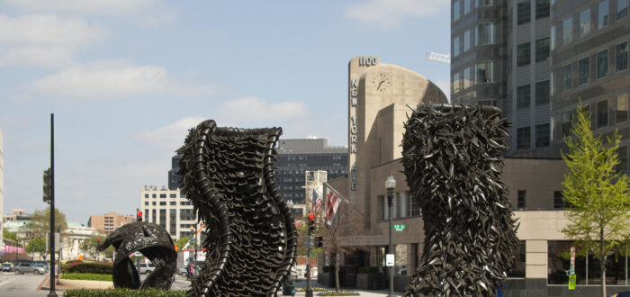 Two large abstract sculptures made from tires rise from a center median in a city street. The sculptures are wavy columns.