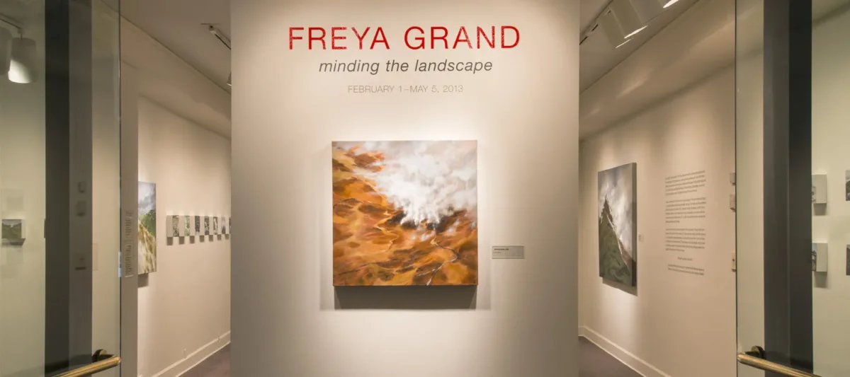 View of an installation. A large painting of a rock formation is hanging on a white wall under the text: "Freya Grand."