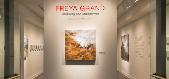View of an installation. A large painting of a rock formation is hanging on a white wall under the text: "Freya Grand."