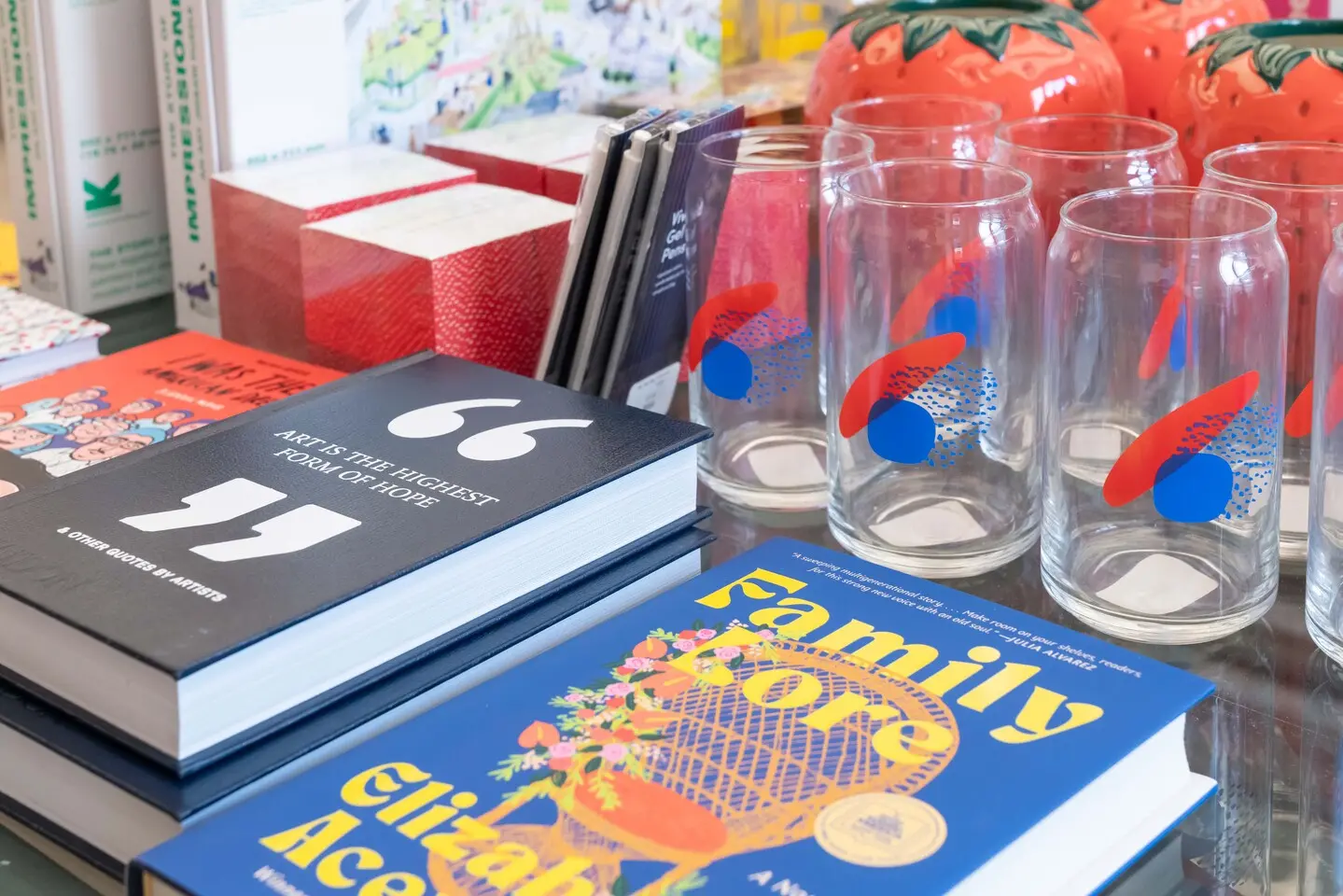 A close up of shop items, including glasses with colorful print and books such as "Family Lore" and "Art is the Highest Form of Hope."