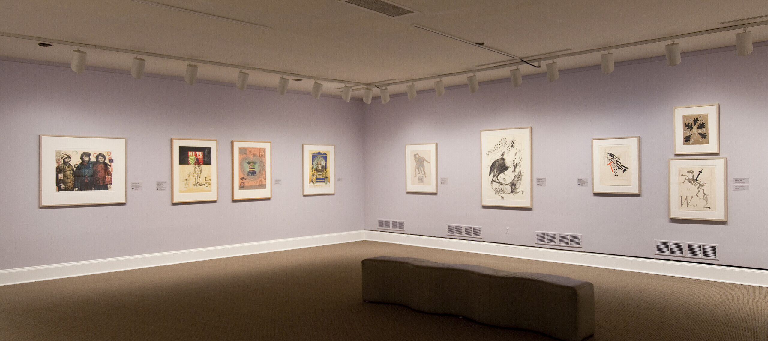 View of an exhibition space with white and lilac walls. There are several prints and lithographs hanging on the walls.