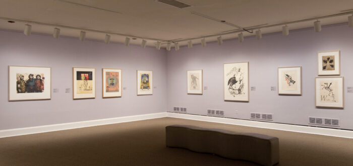 View of an exhibition space with white and lilac walls. There are several prints and lithographs hanging on the walls.
