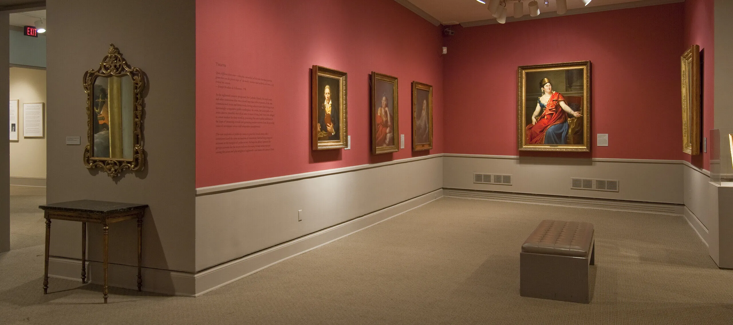 View of a gallery space with red walls. A golden mirror with plenty of ornaments is hanging to the left, large historical portraits of women are hanging to the right.