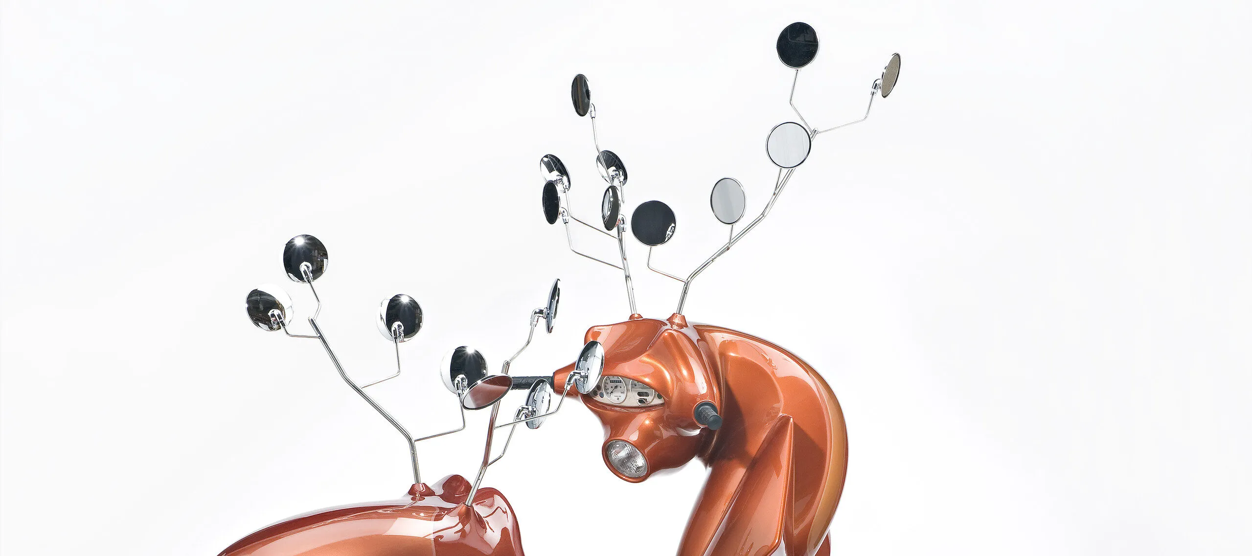 A sculpture consists of two metallic-orange motor scooters manipulated to resemble male deer. Leather seats become haunches, dashboard dials resemble faces, and multiple rear-view mirrors morph into antlers. The serpentine, hybrid animal-machines appear to spar for dominance.