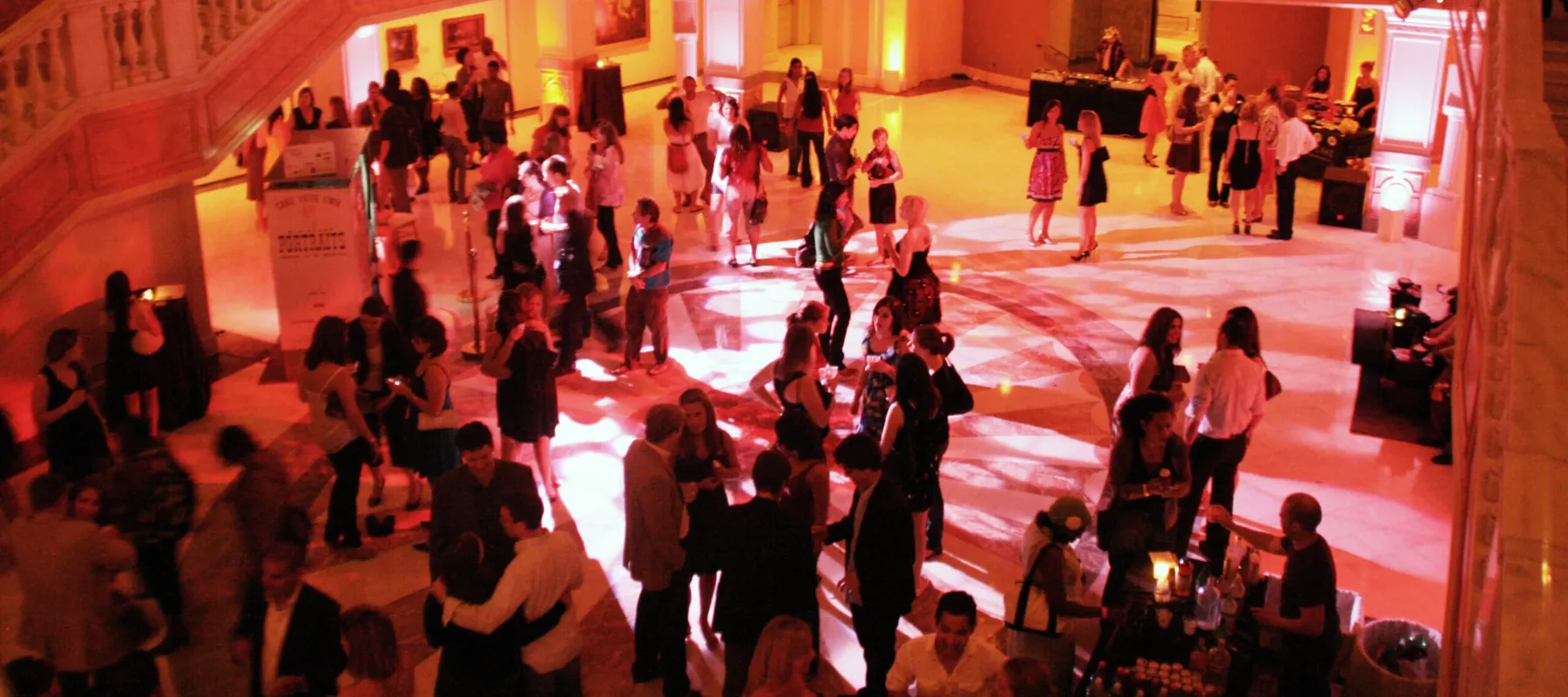 A grand entrance hall lit with an amber glow is filled with attendees during an evening event at the museum.