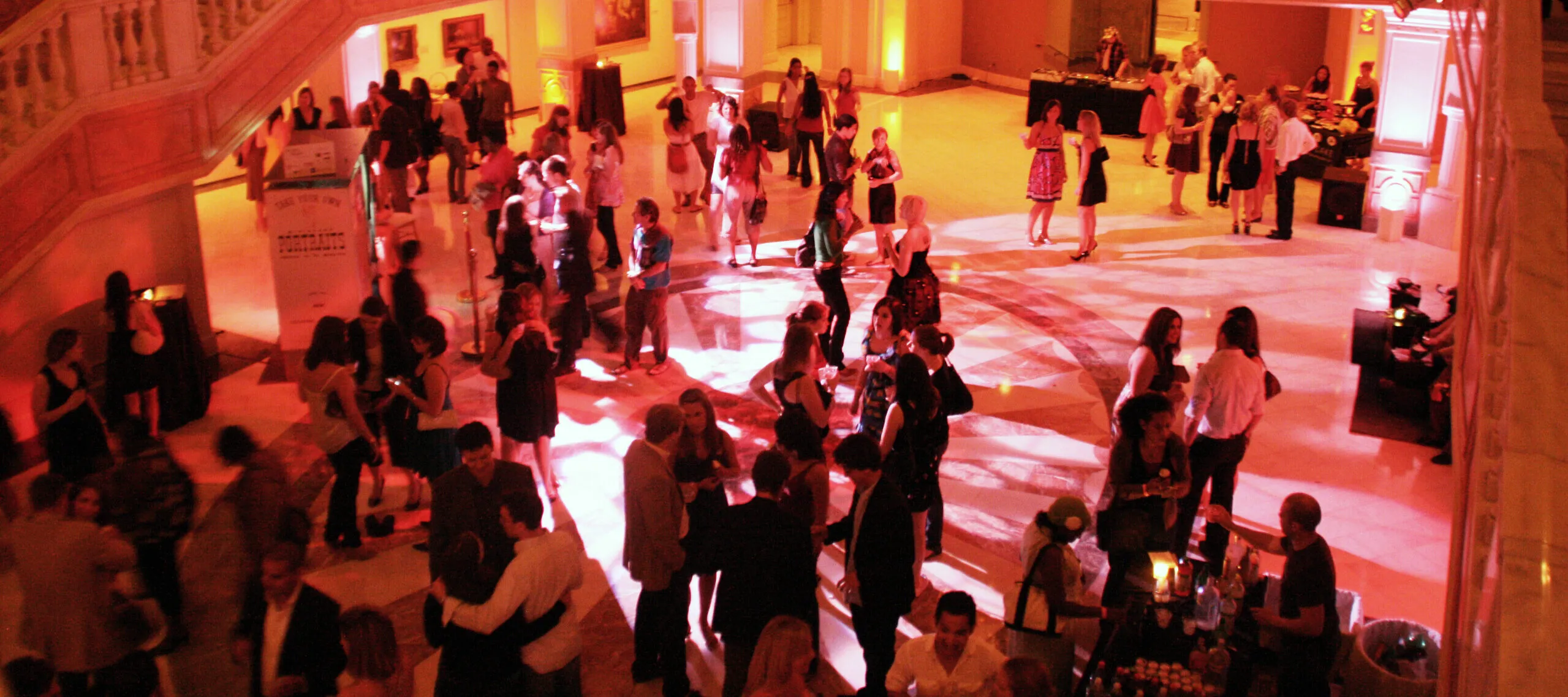 A grand entrance hall lit with an amber glow is filled with attendees during an evening event at the museum.