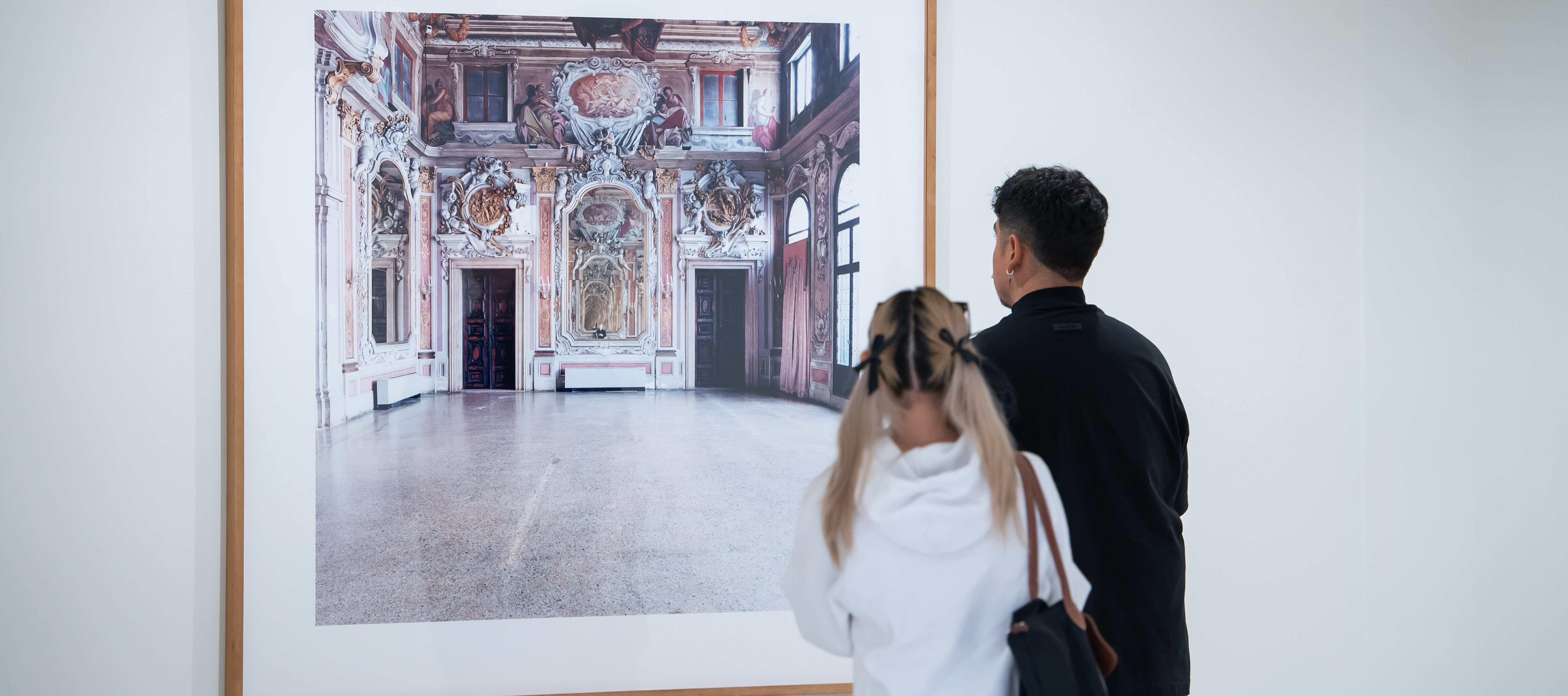 Two museum visitors observe a large artwork on the wall.