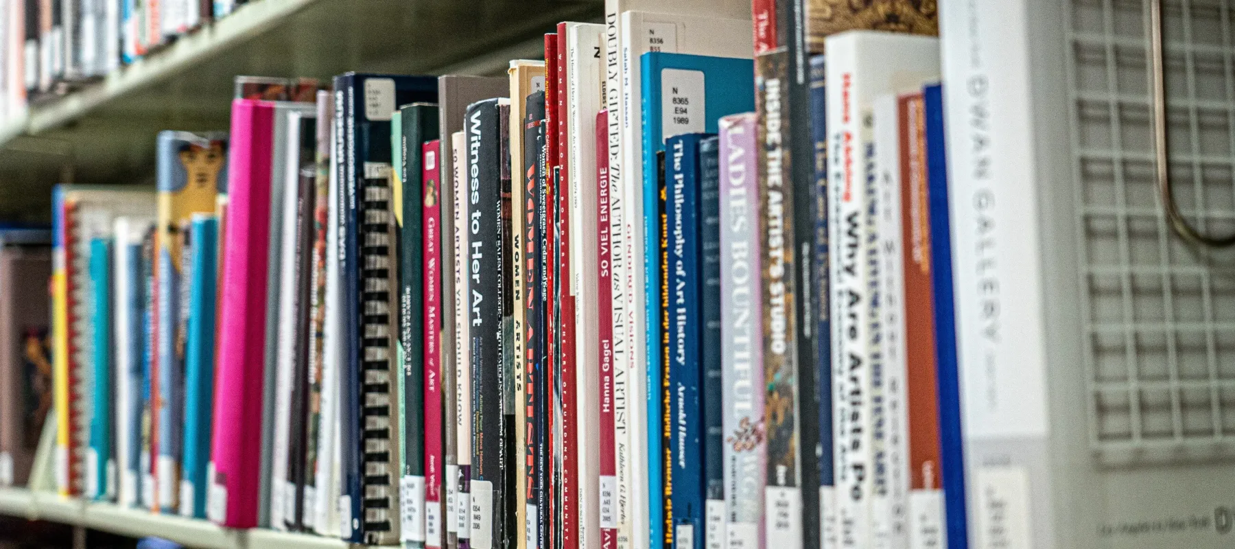 A bookshelf packed with colorful books about women artists.