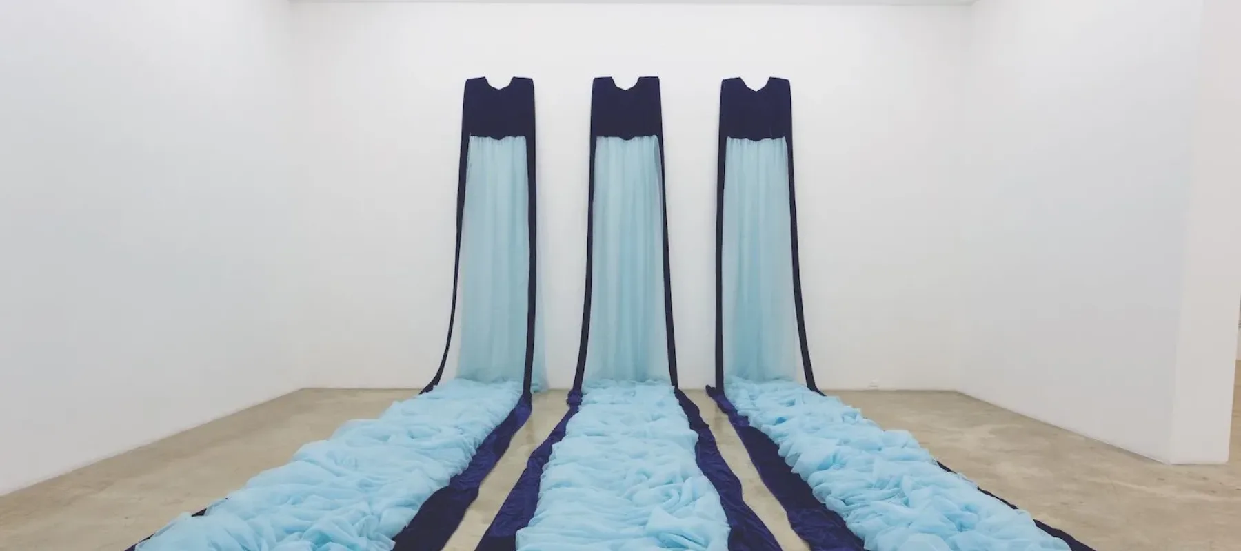 Three long fabric trains in two shades of blue, mounted on a far wall and cascading onto the floor like a waterfall.