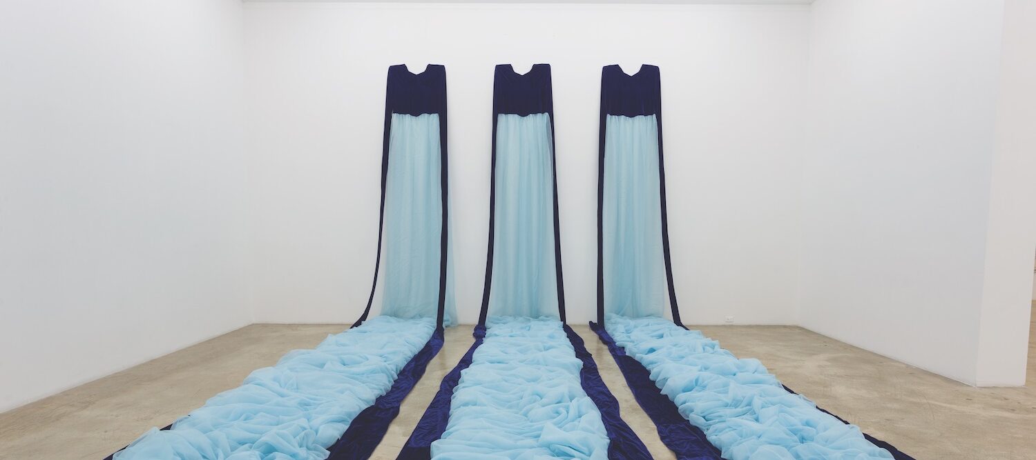 Three long fabric trains in two shades of blue, mounted on a far wall and cascading onto the floor like a waterfall.