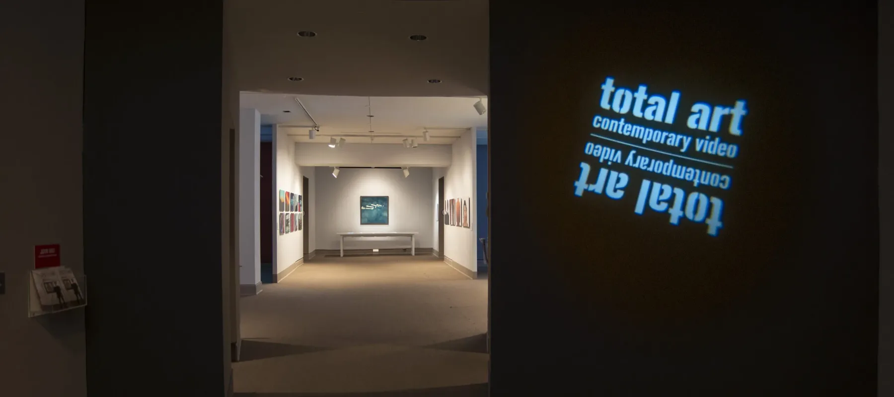 View of a gallery space. In a dark room, the title of the exhibition, "Total Art: Contemporary Video", is projected on a wall.