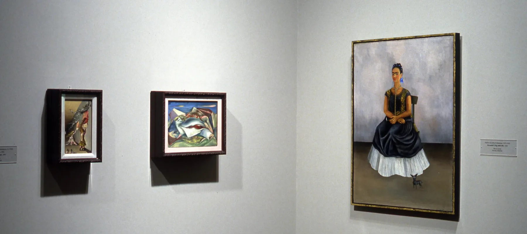 A portrait of a woman with a light skin tone is hanging on the wall to the right, and two small Surrealist works are hanging to the left.