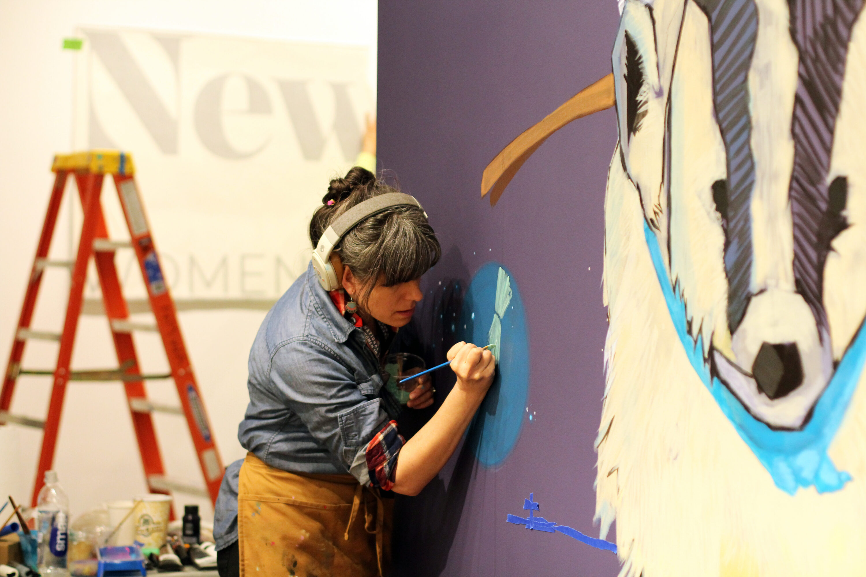A woman artist paints a mural on a wall of a museum gallery.