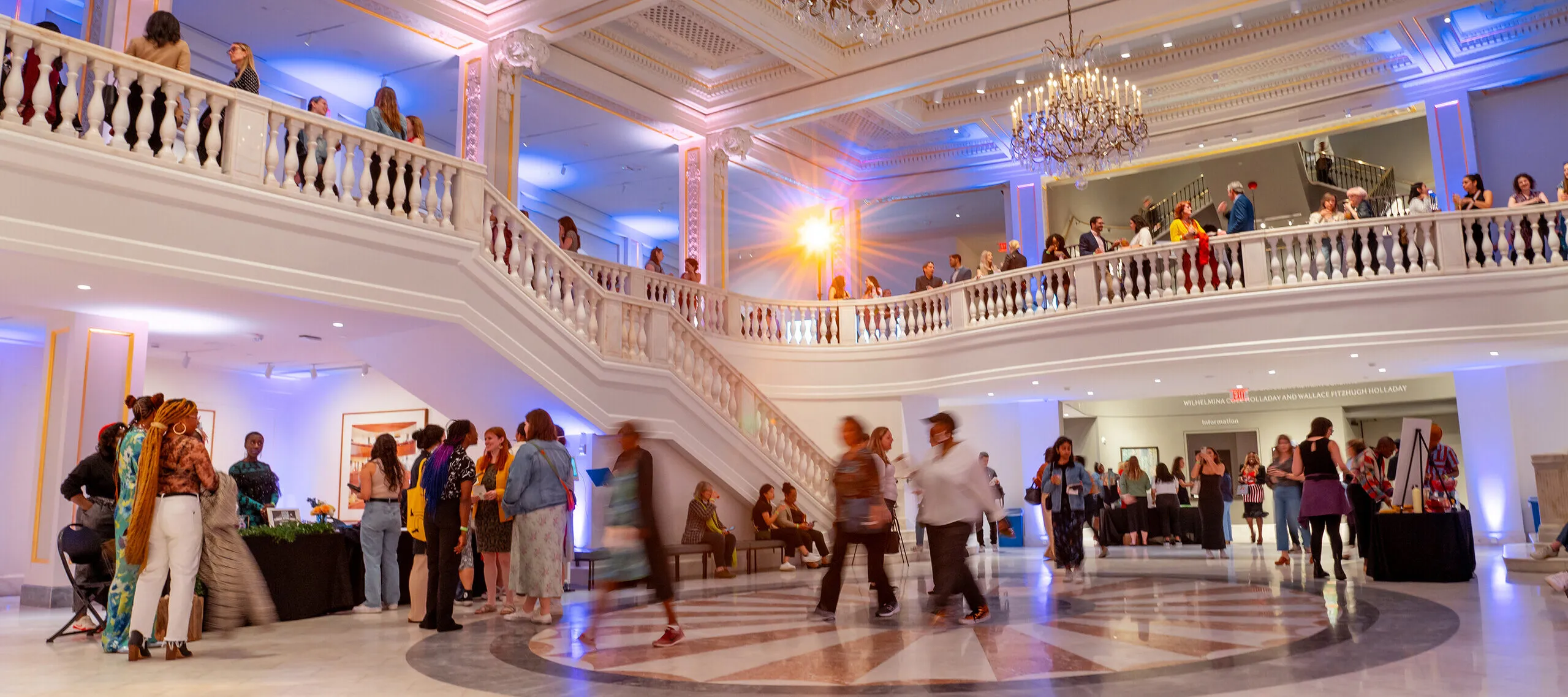 Groups of people enter a large white, marble room.