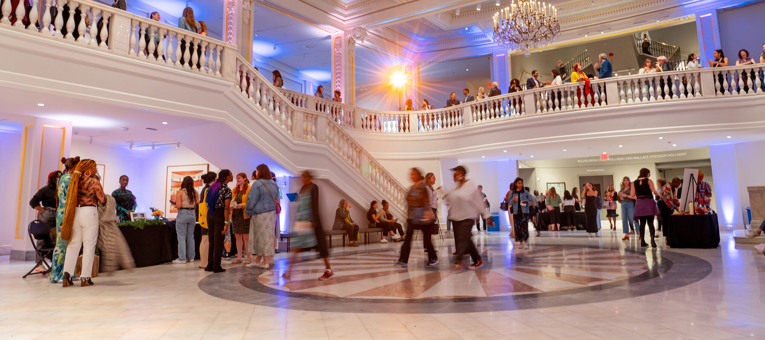 Groups of people enter a large white, marble room.