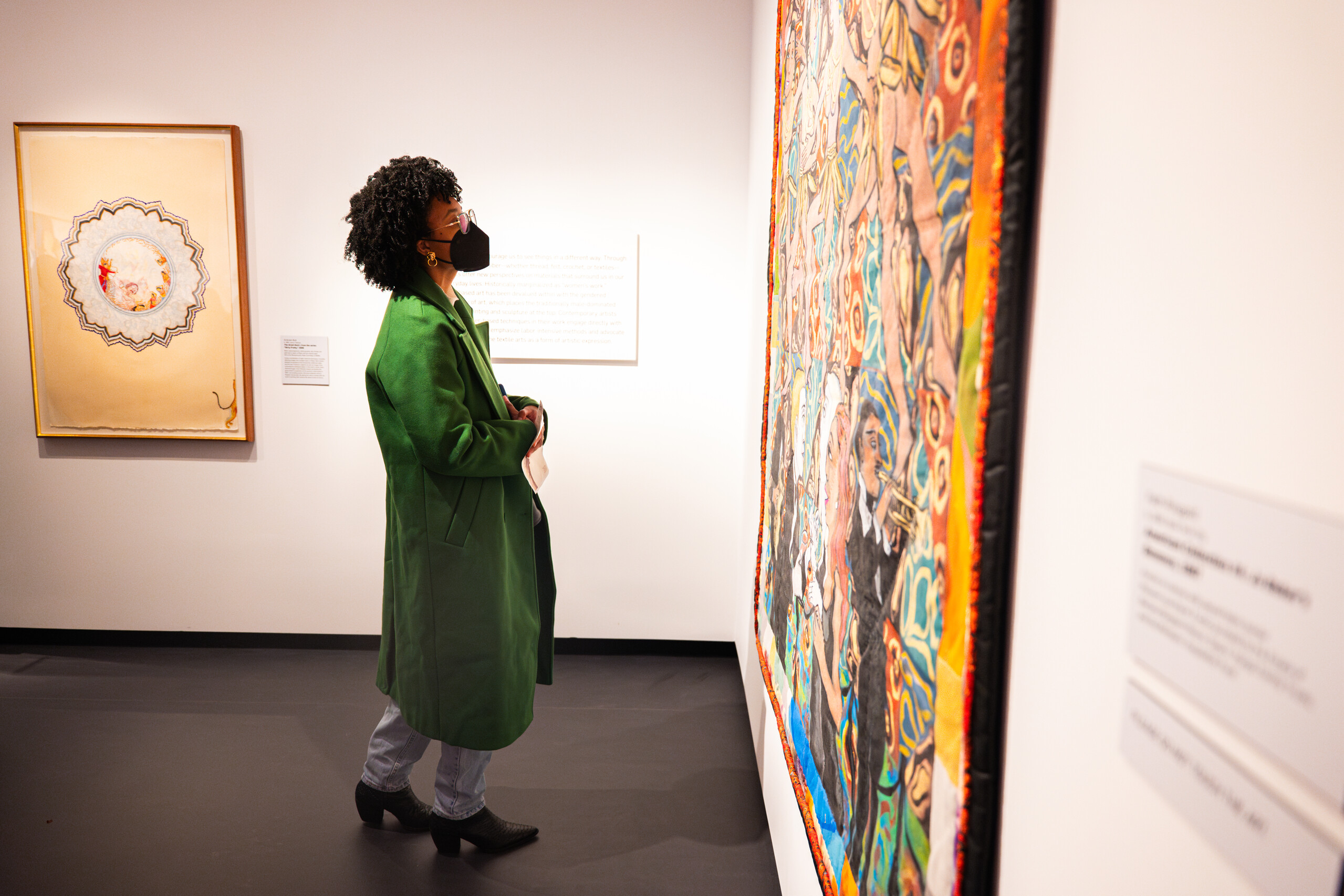 A woman in a green coat looks at a colorful painting