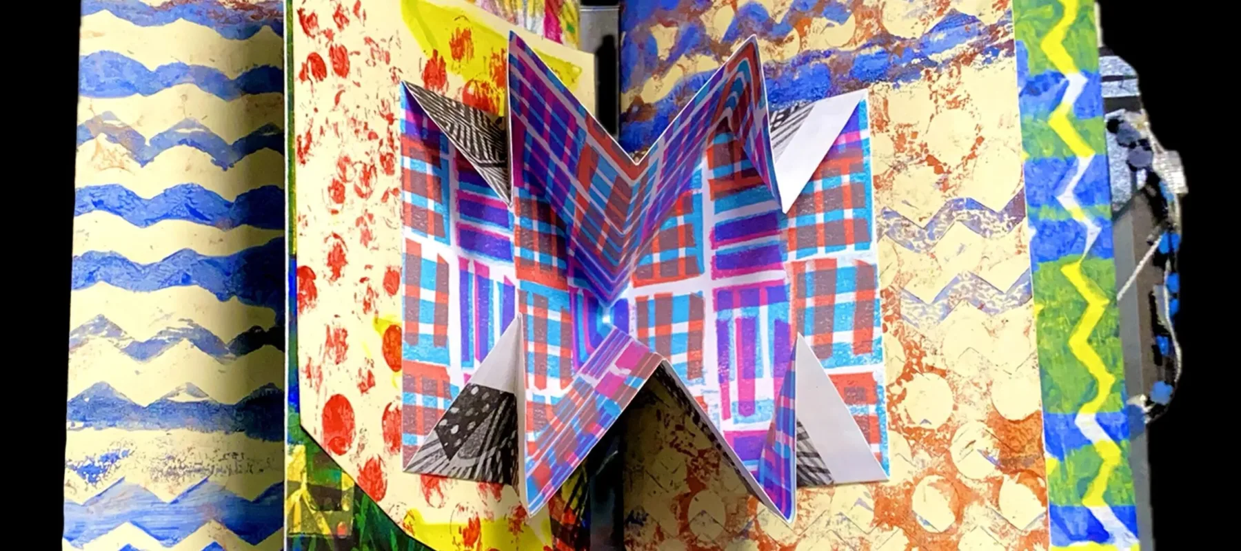 An open open book with a pop-up element in the center spread. Several pages of the book are visible, and each has a different, brightly patterned design printed on it.