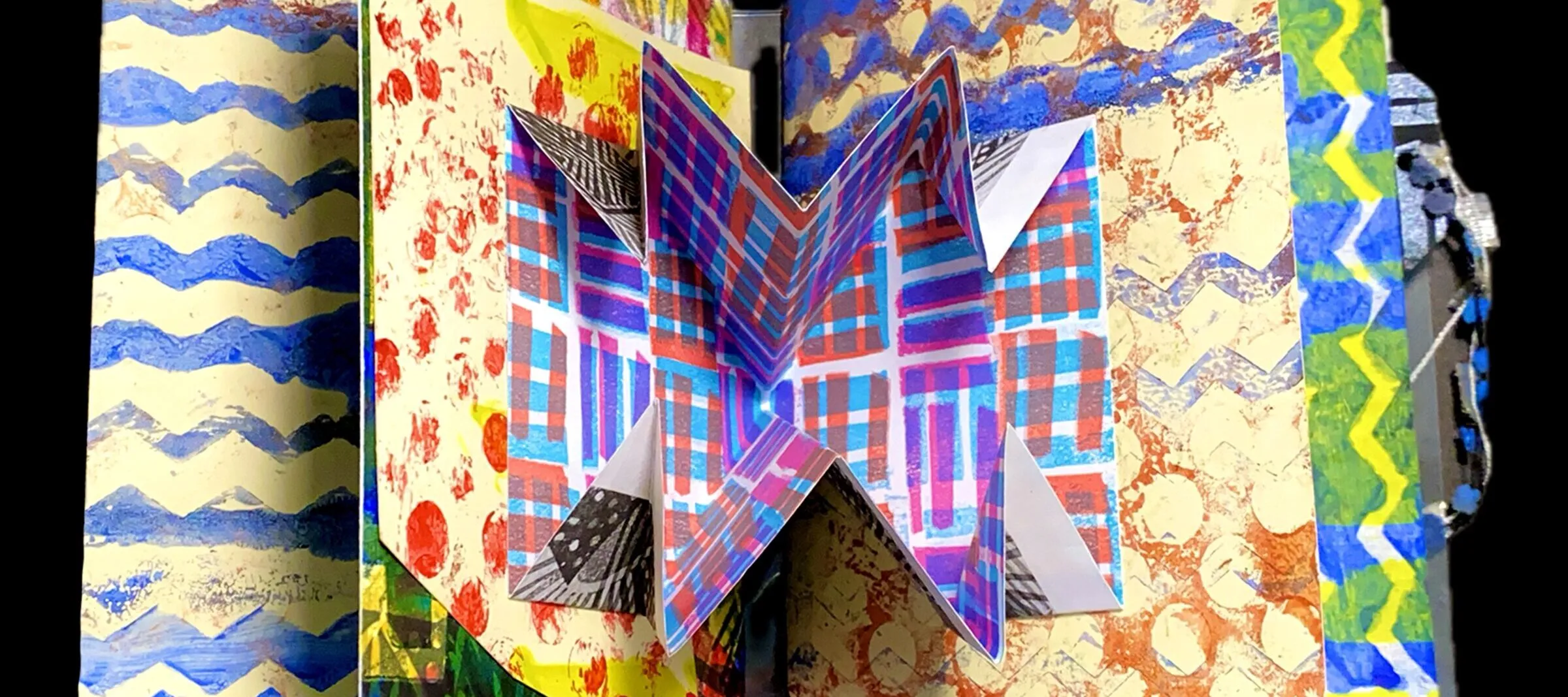 An open open book with a pop-up element in the center spread. Several pages of the book are visible, and each has a different, brightly patterned design printed on it.