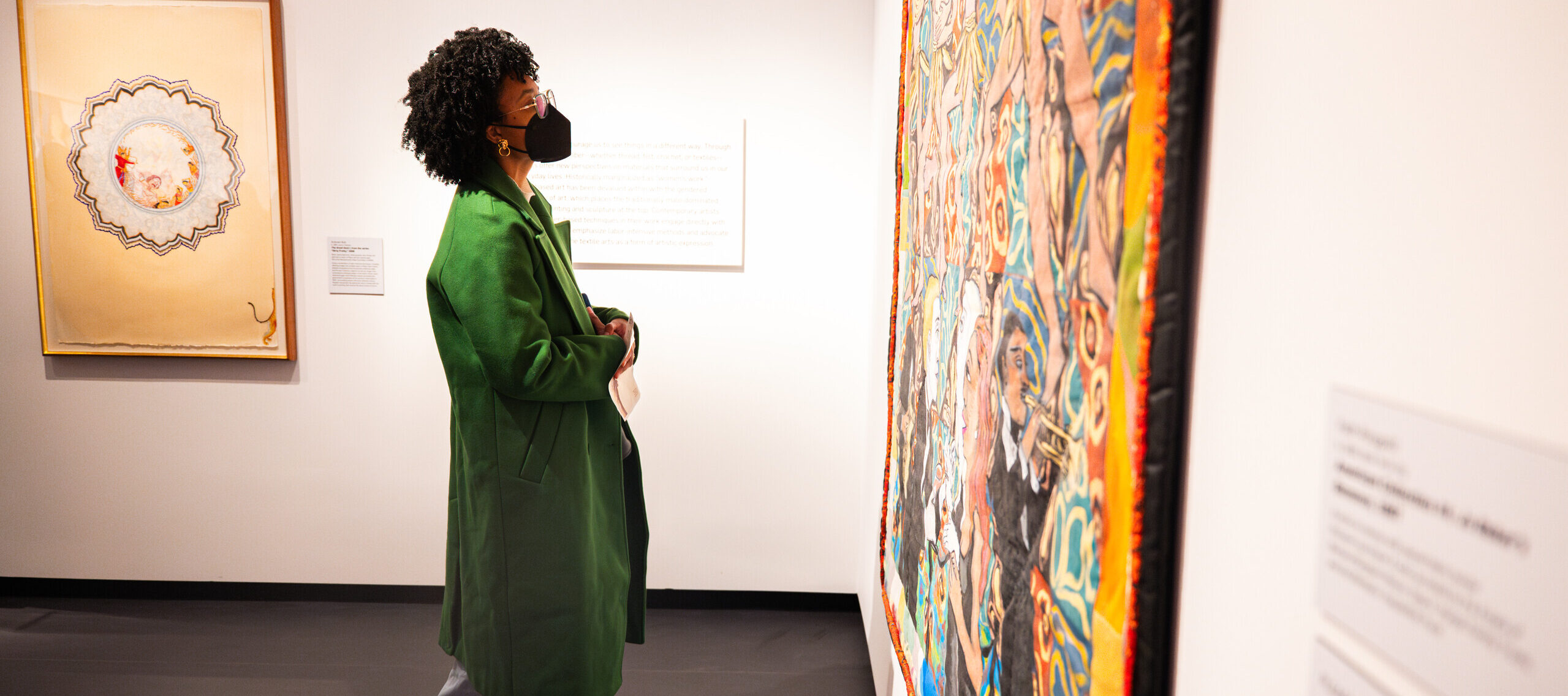 A woman in a green coat looks at a colorful painting