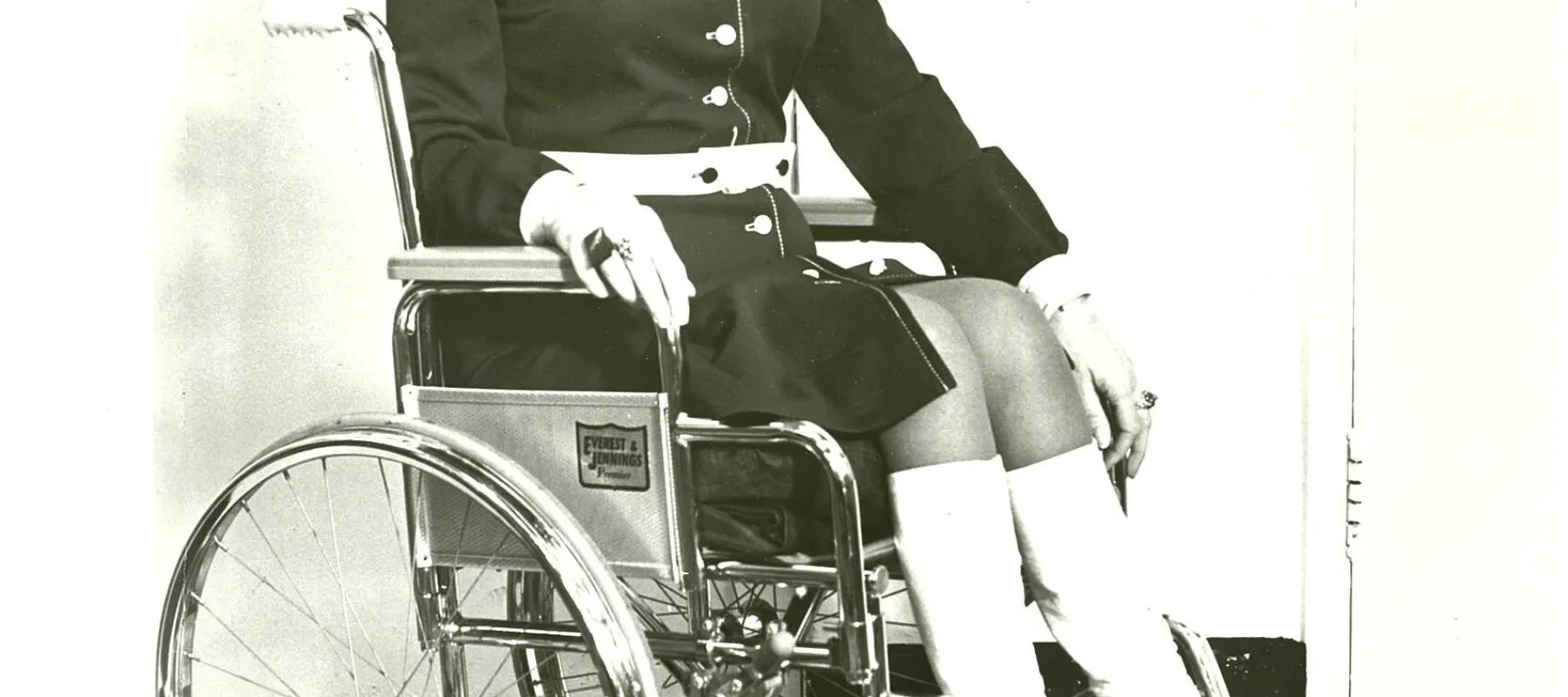 A black-and-white photo of a woman in a wheelchair wearing stylish 1970s dress.