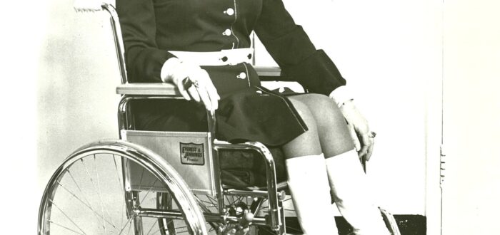 A black-and-white photo of a woman in a wheelchair waring stylish 1970s dress.