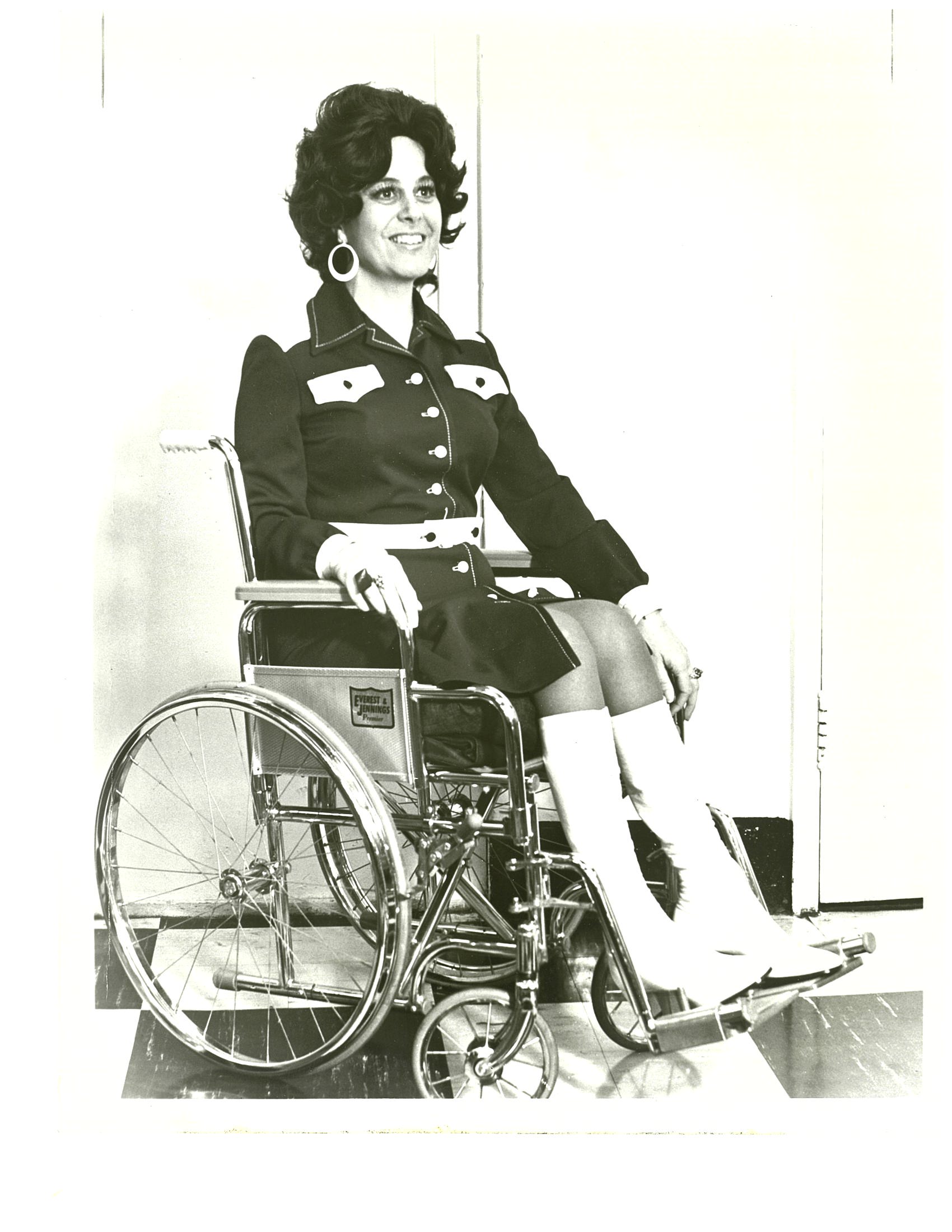 A black-and-white photo of a woman in a wheelchair wearing stylish 1970s dress.