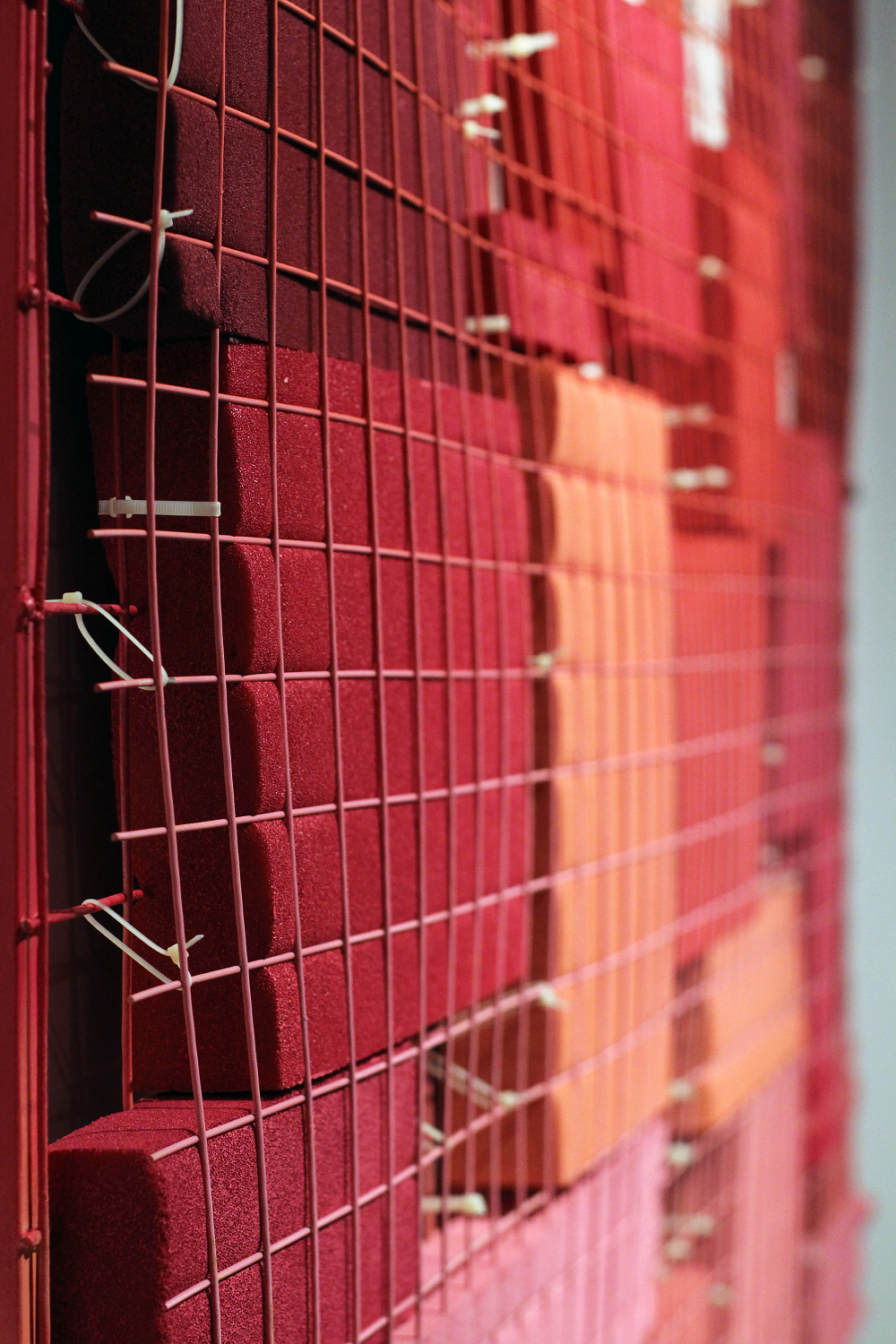 A close-up photograph of a geometric abstraction featuring red, orange, and pink rectangles sandwiched between red grates.