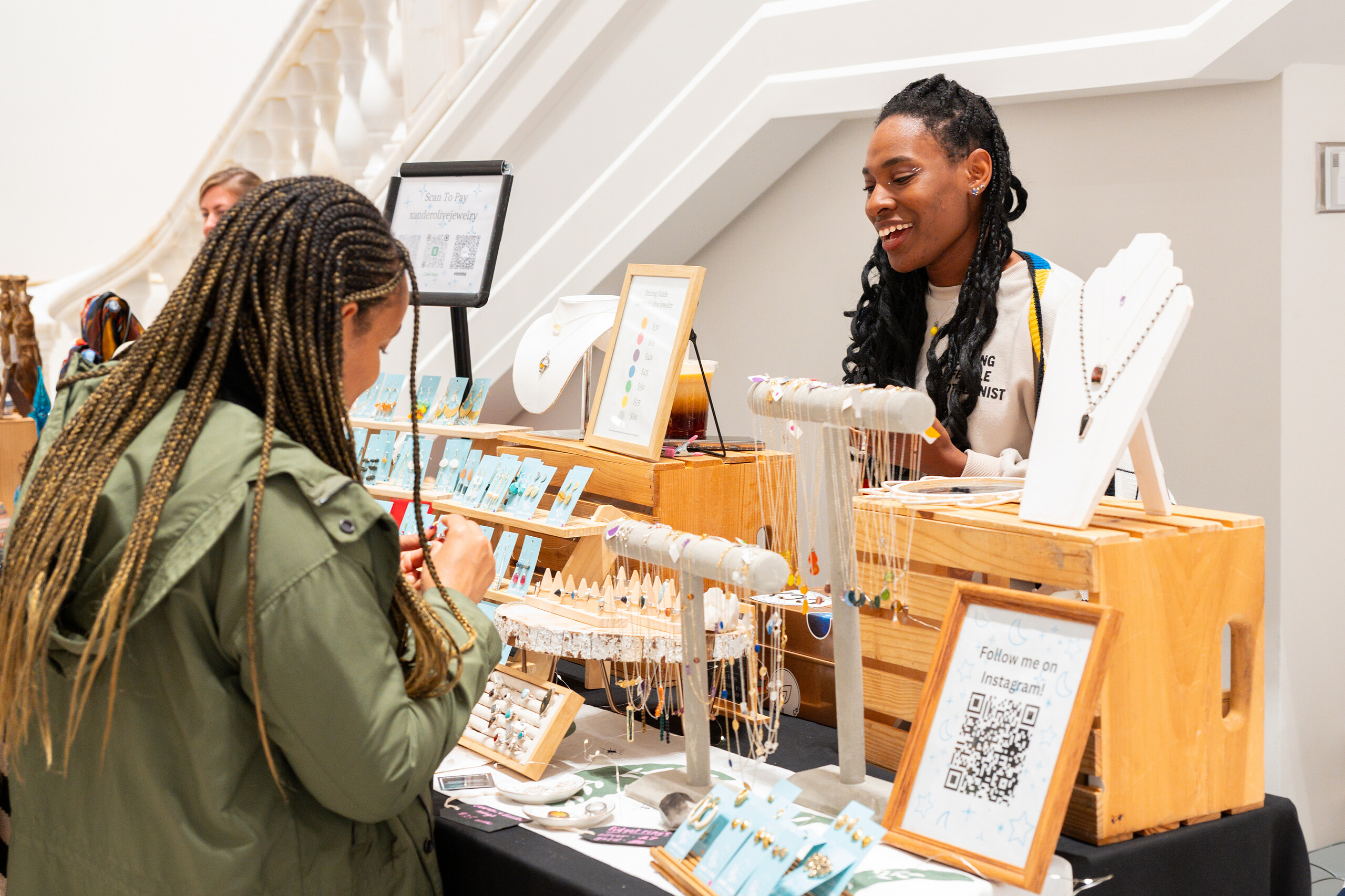 A woman in a green jacket looks at a table displaying jewelry.