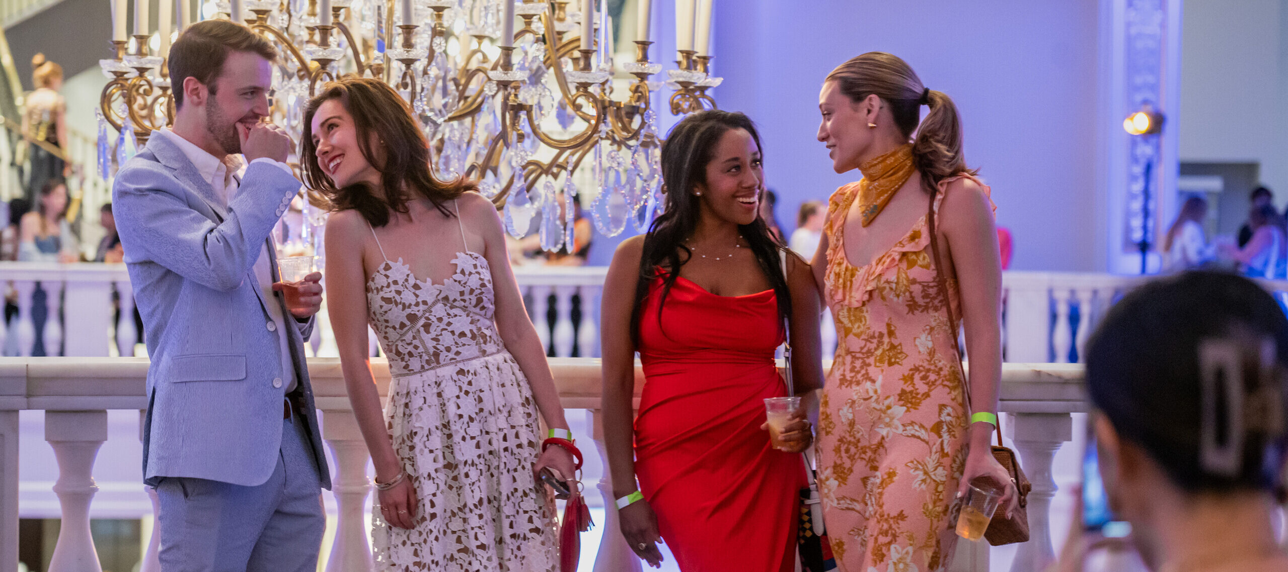 A man and three women all in semiformal attire talk to each other as they pose for a picture.